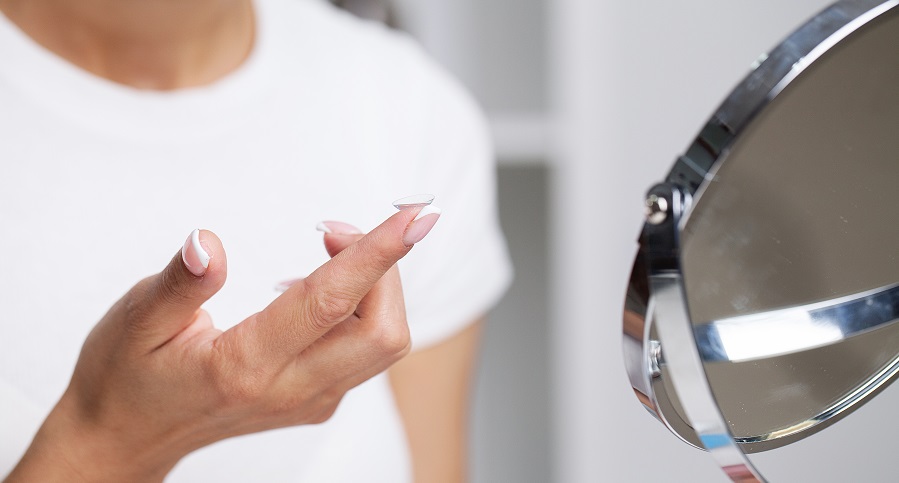 Kobieta zakładająca soczewki kontaktowe przed lustrem.